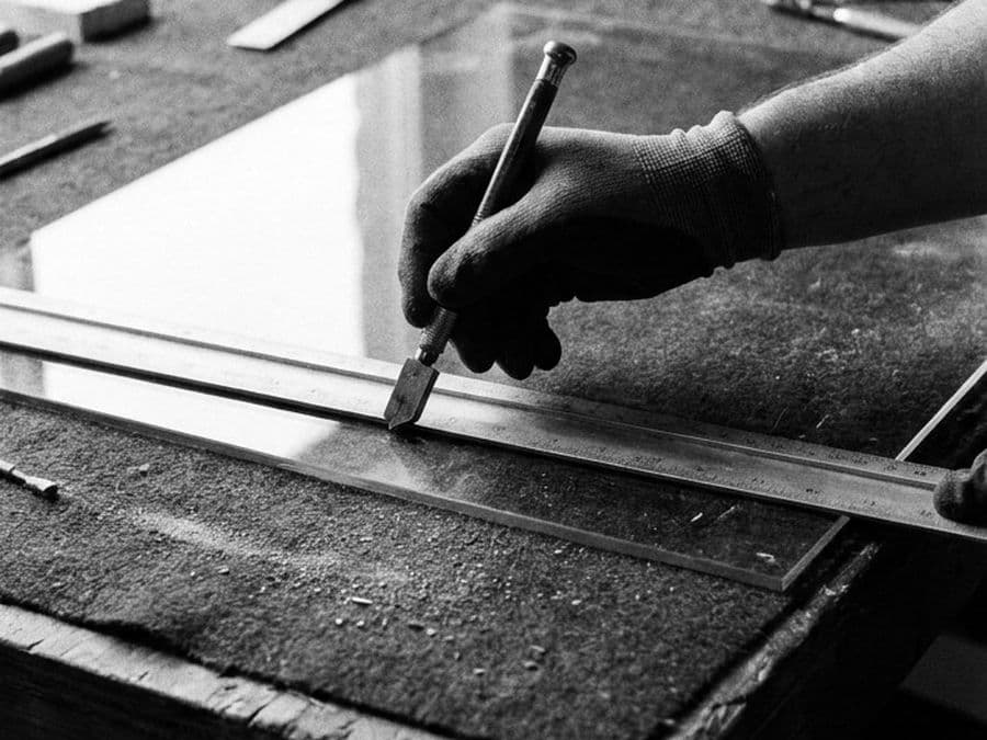A hand scoring a sheet of glass along a straight edge.