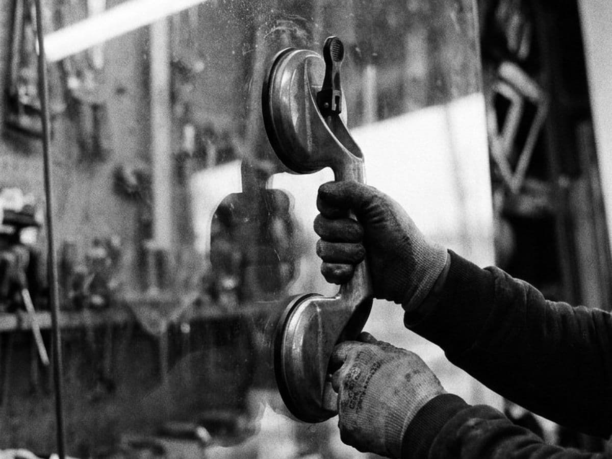 Gloved hands lifting a sheet of glass with a suction lifter.