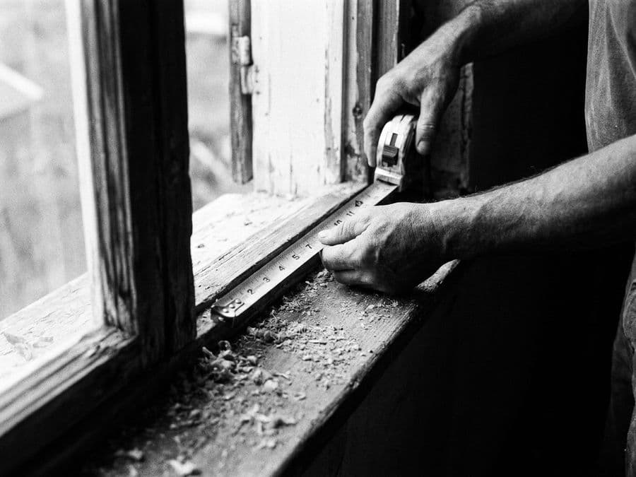 Hands running a tape measure across a window frame.